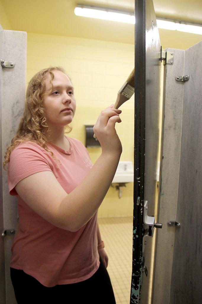 Junior Bella Friedhoff brushes the door of one of the stalls in the girls bathroom. The SGA is in the process of planning a renovation of the doors to brighten up the space. Photo by Masako Kaneko.