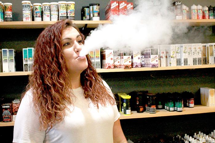 Janty Vapors employee Brylee McFadden vapes at her store. McFadden explained that the size of small vapes are more attractive to younger customers. Photo by Allison McCauley-Cook.